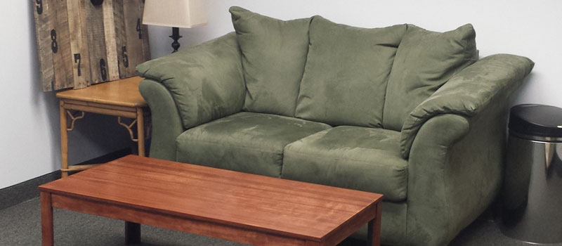 Green comforable looking couch with a wooden coffee table in front of it