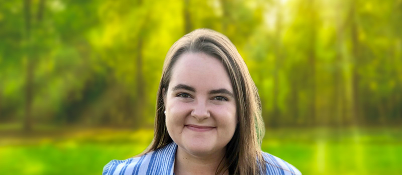 Katie Stephenson wearing a blue striped blouse with woods and grass in the background